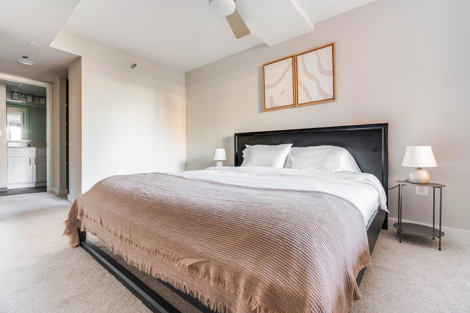 Un dormitorio con cama, lámparas de noche, cabecera y una puerta que da a un baño.