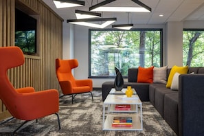 A modern living room with a large window, orange chairs, a gray sofa, and a white coffee table with books. - Blueground | Clarendon, pool, nr Arlington Cemetery (Arlington)