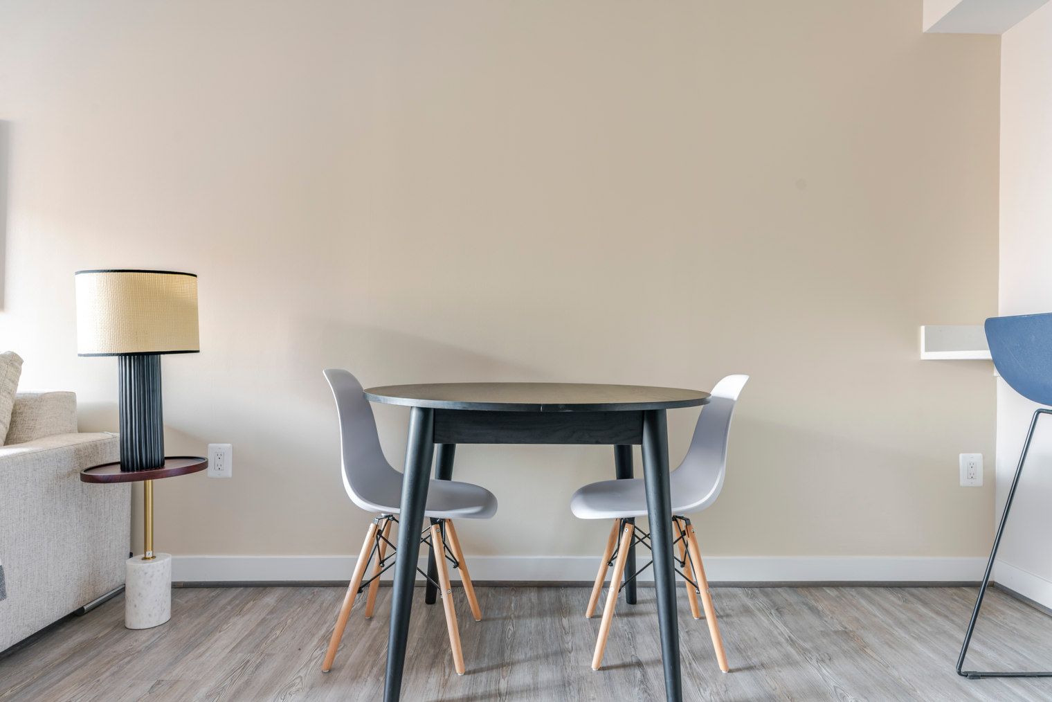 A modern dining area with a round table and two chairs, a lamp, and a sofa.