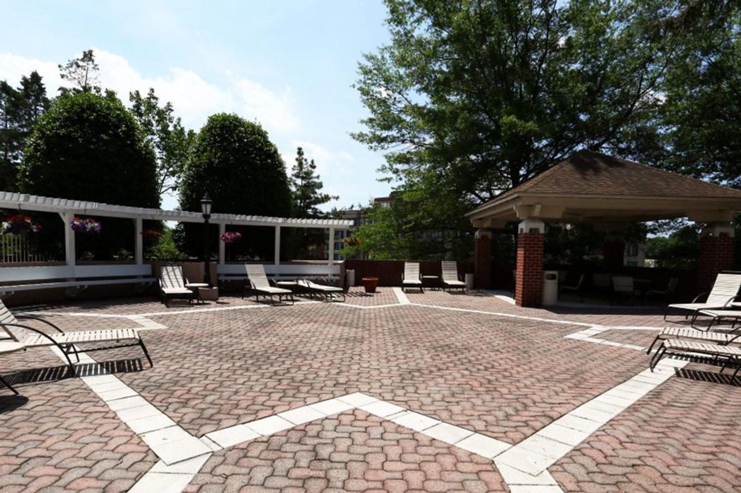 A covered outdoor area with brick flooring, lounge chairs, and a gazebo.