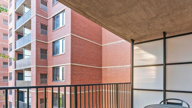 En bygning med flere etager, en murstensfacade, en balkon med gelænder og et vindue med udsigt til bygningens indre.