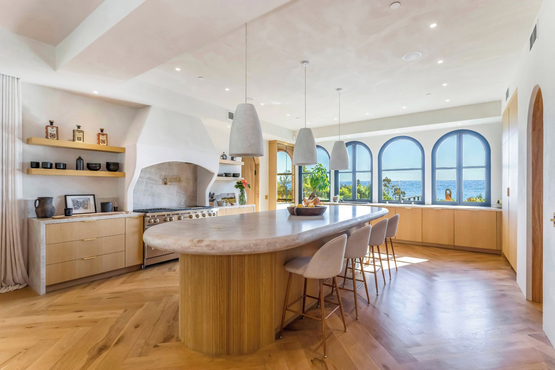 Cozinha moderna com ilha central, luminárias pendentes e amplas janelas com vista.