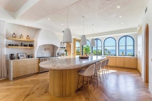 Cozinha moderna com ilha central, luminárias pendentes e amplas janelas com vista.