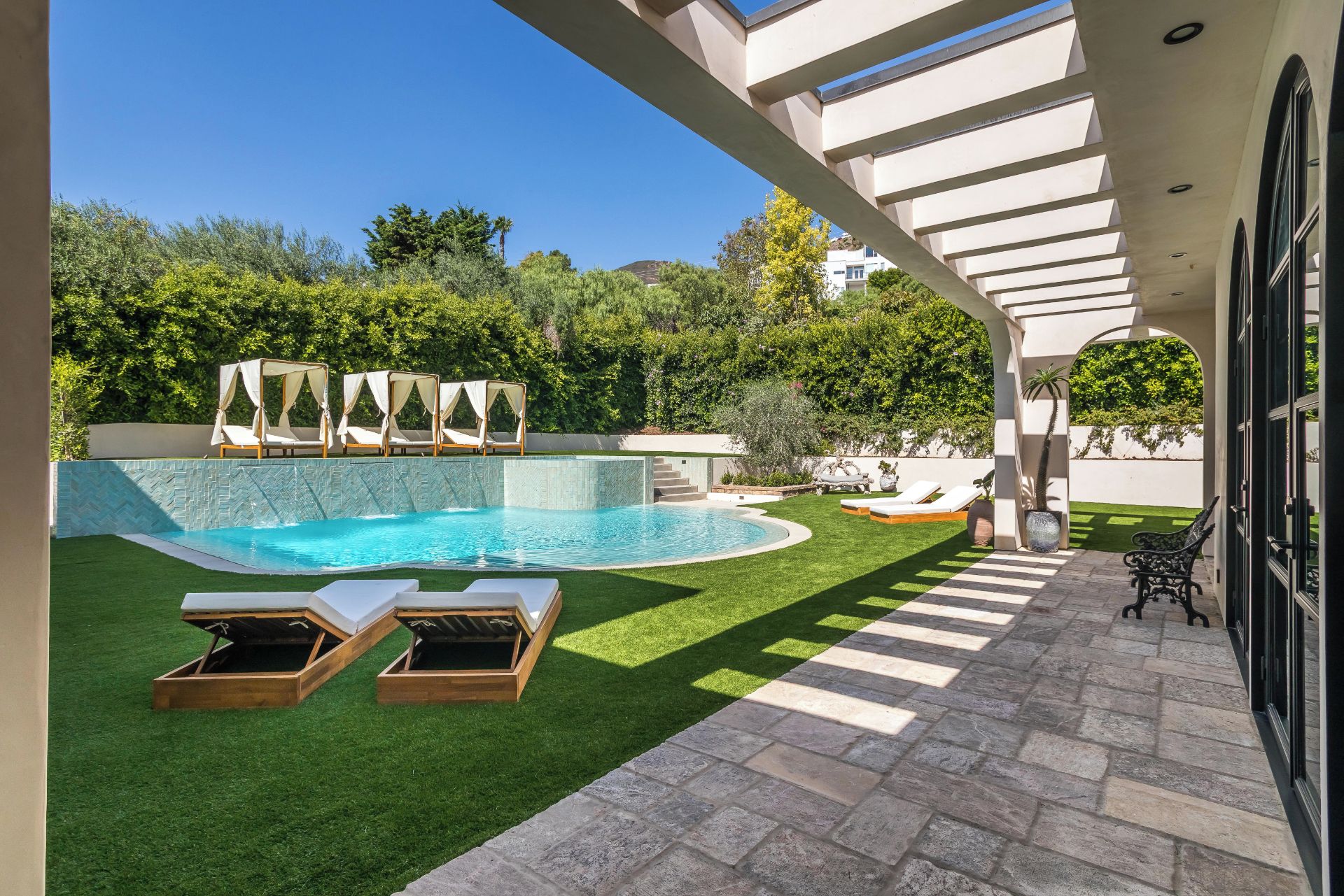 Piscina com deck de pedra, cadeiras de descanso e estrutura de pérgola.
