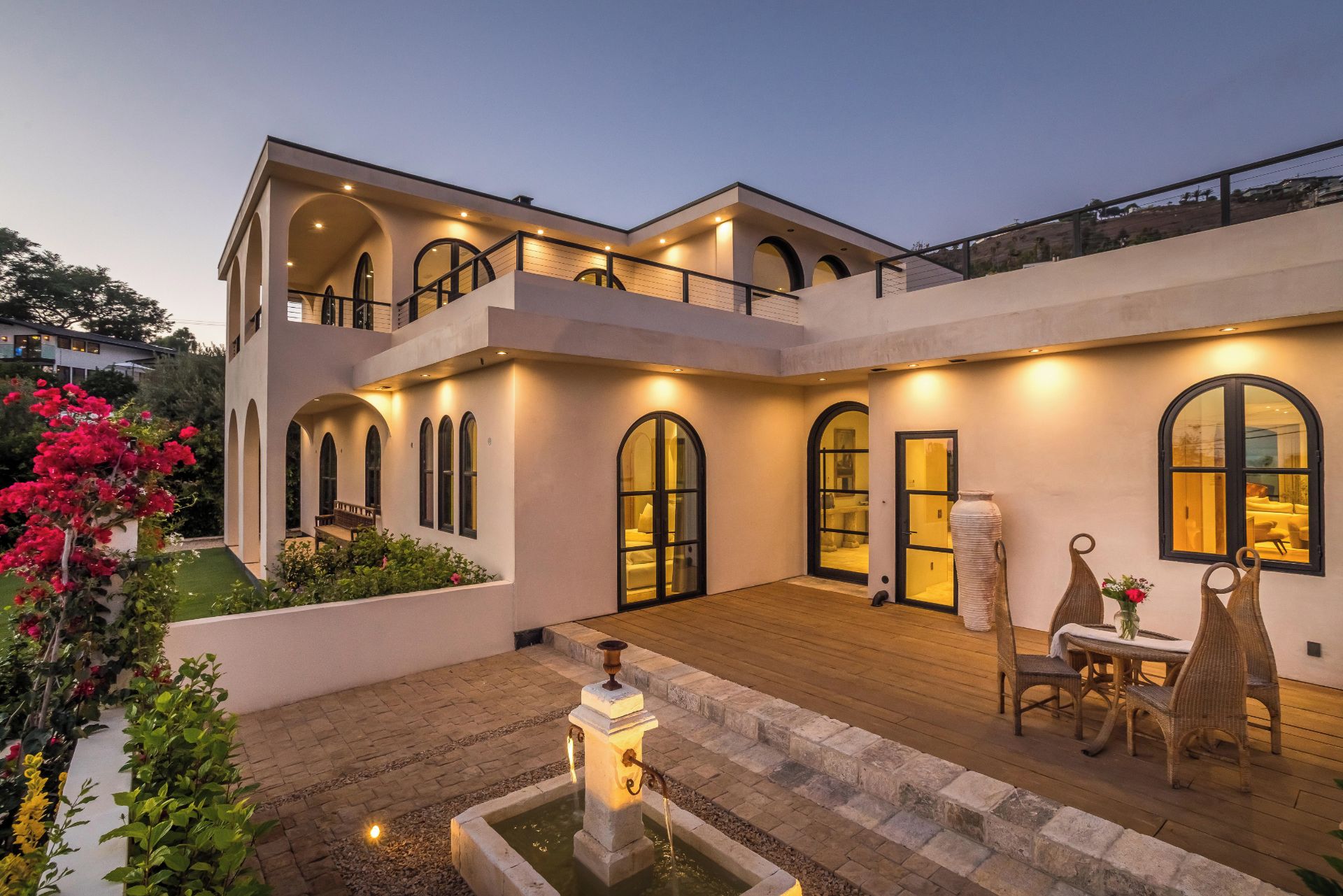 A modern two-story house with a courtyard, a fountain, and outdoor seating.