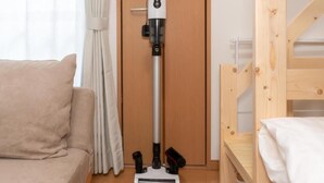 A room with a beige sofa, a wooden bunk bed, and a vacuum cleaner against a wooden door. - Suncity Hakata (Fukuoka City Hakataku  Katakasu)