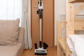 Et værelse med en beige sofa, en køjeseng i træ og en støvsuger op ad en trædør.