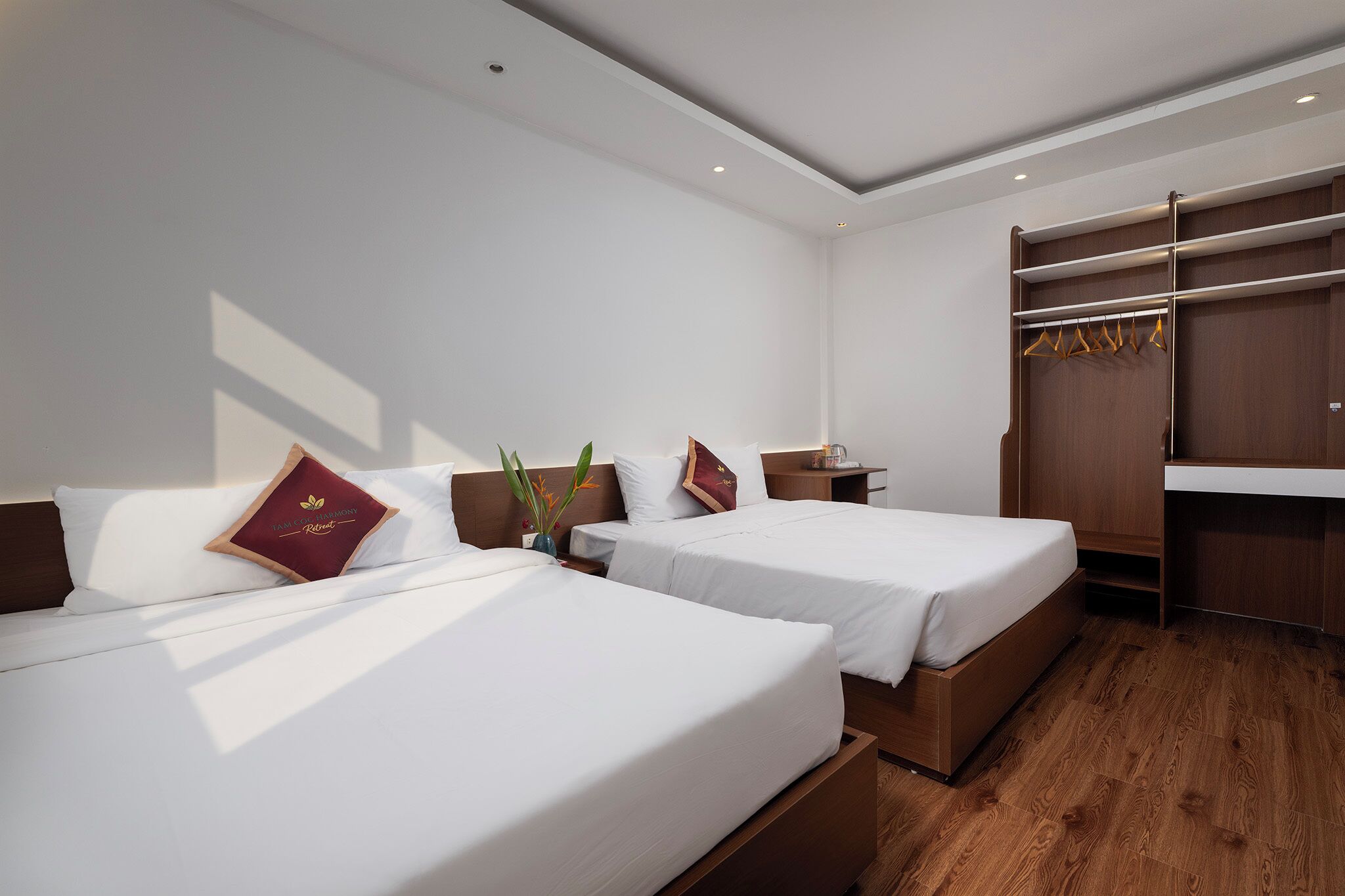 A hotel room with two beds, a wooden wardrobe, and a small desk.