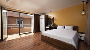 Una camera d'albergo con un letto grande, una scrivania, una sedia, un armadio e un balcone con ringhiera.