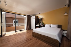 A hotel room with a large bed, a desk, a chair, a wardrobe, and a balcony with a railing. - Harmony Retreat Ninh Binh (Nam Hoa Lu)