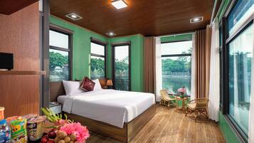 A hotel room with a large bed, a dining table with chairs, a view of a body of water, and a balcony.