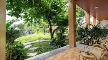 Un espacio al aire libre techado, con piso de madera, sendero de piedra y abundante vegetación.