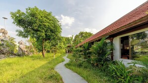 Un sentiero conduce a un edificio con tetto in tegole, immerso nel verde e affiancato da una struttura in pietra.