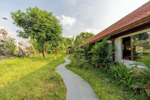 A pathway leading to a building with a tiled roof, surrounded by lush greenery and a stone structure. - Harmony Retreat Ninh Binh (Nam Hoa Lu)