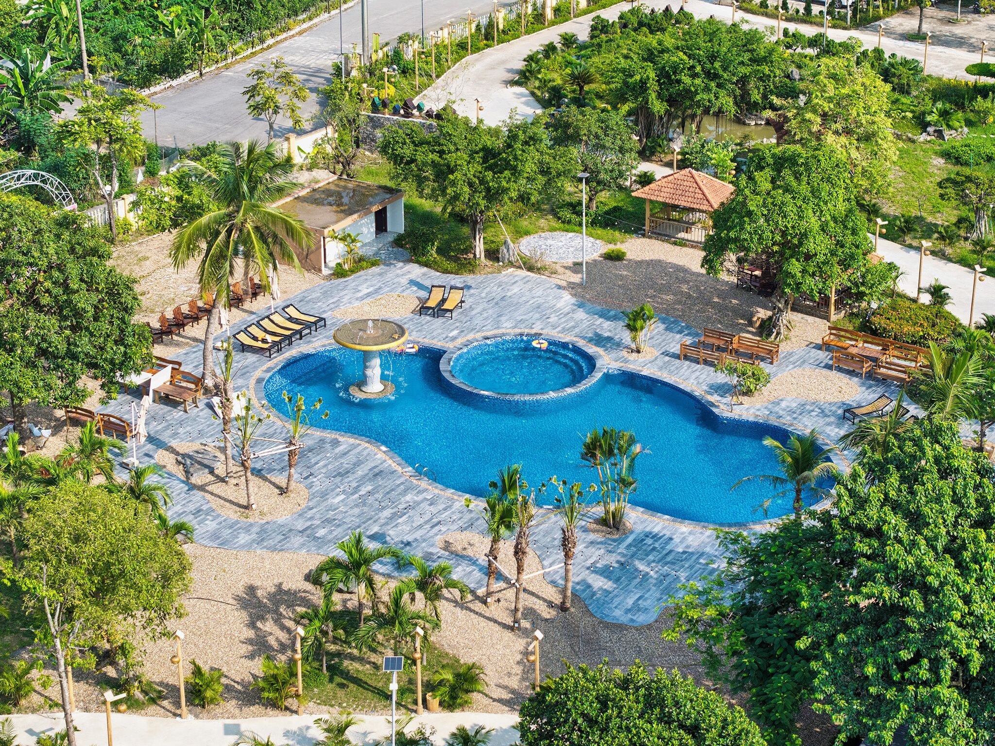 A large outdoor swimming pool with multiple seating areas and a fountain, surrounded by palm trees and greenery.