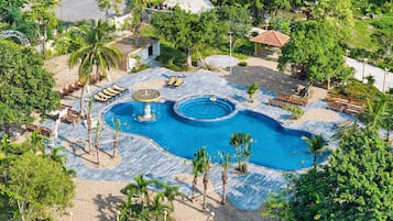 A large outdoor swimming pool with multiple seating areas and a fountain, surrounded by palm trees and greenery.