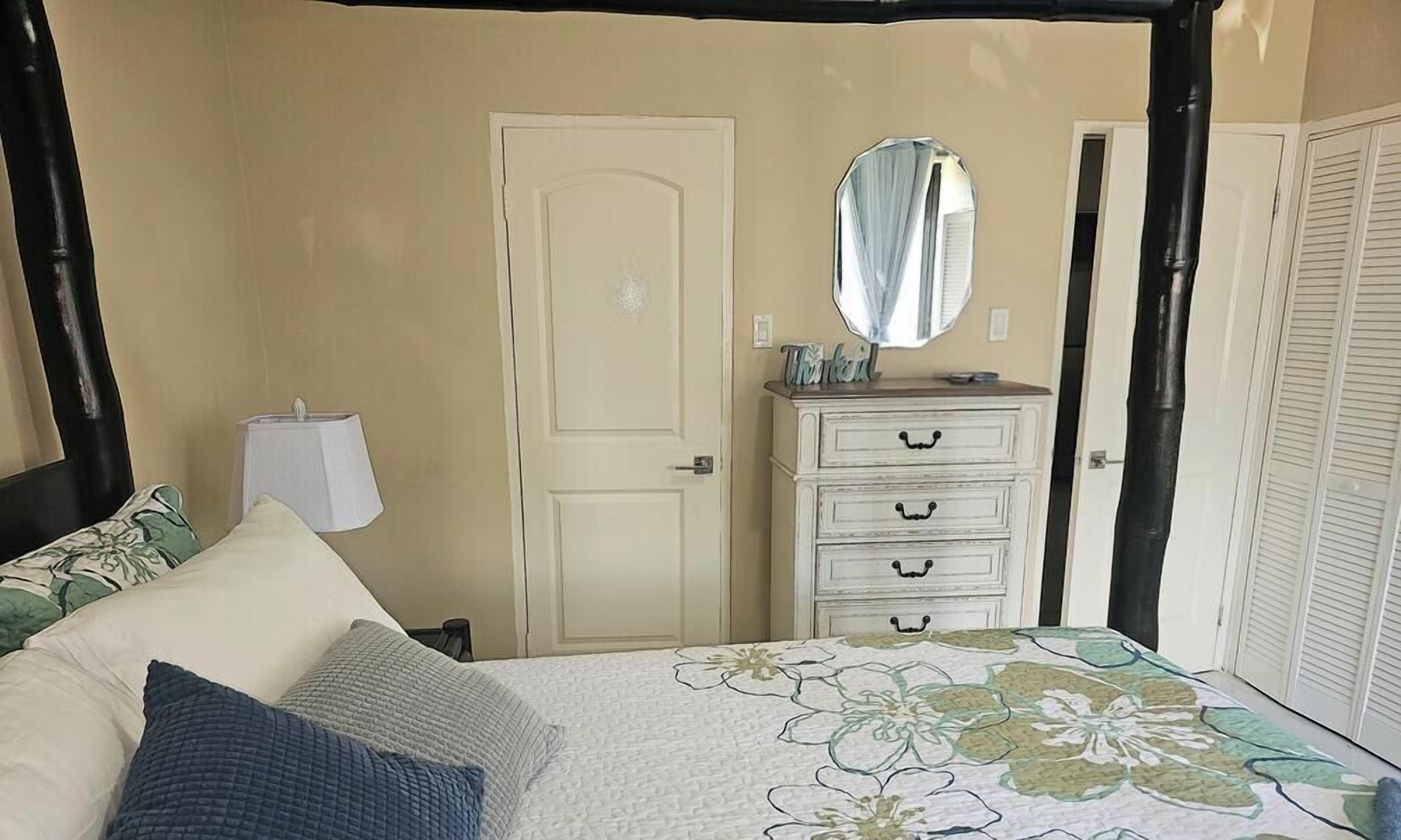 A bedroom with a bed, a dresser, a mirror, and a door.