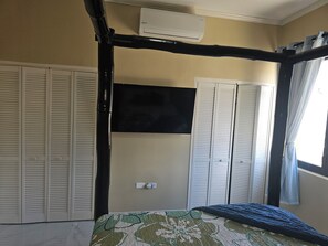 Een slaapkamer met een bed, een kledingkast, een raam met gordijnen en een airconditioning.
