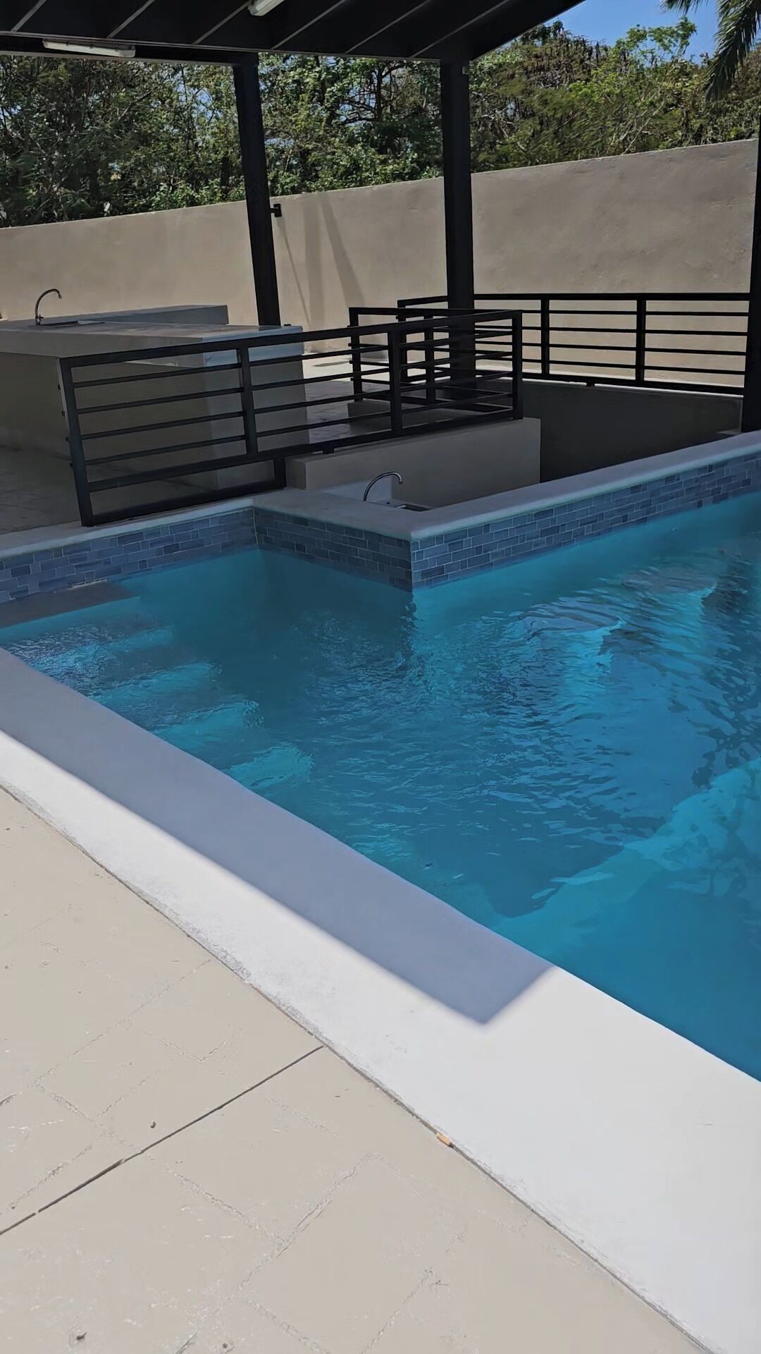 A swimming pool with a tiled edge, a metal railing, and a covered seating area.