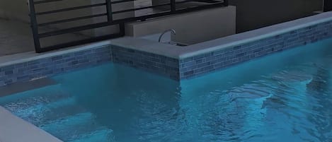 A swimming pool with a tiled edge, a metal railing, and a covered seating area.
