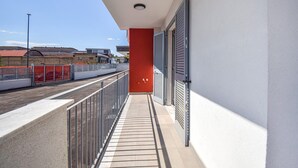 Een balkon met een metalen hekwerk, een rode muur en uitzicht op een straat met gebouwen en een schutting.