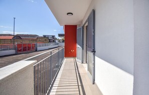 A balcony with a metal railing, a red wall, and a view of a street with buildings and a fence. - 2 bedroom gorgeous apartment in Casoria (Casoria)