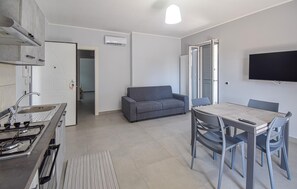 A modern kitchen with a gas stove, a built-in oven, and a sink. There is a gray sofa and a dining table with chairs in the living area.