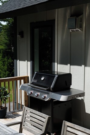An outdoor grill with four control knobs, a digital display, and a logo on the side, set on a wooden deck with a potted plant and a chair. - Luxe Windham - Hot Tub, Views, Firepit, Peloton - 5min to Mountain! (Windham)