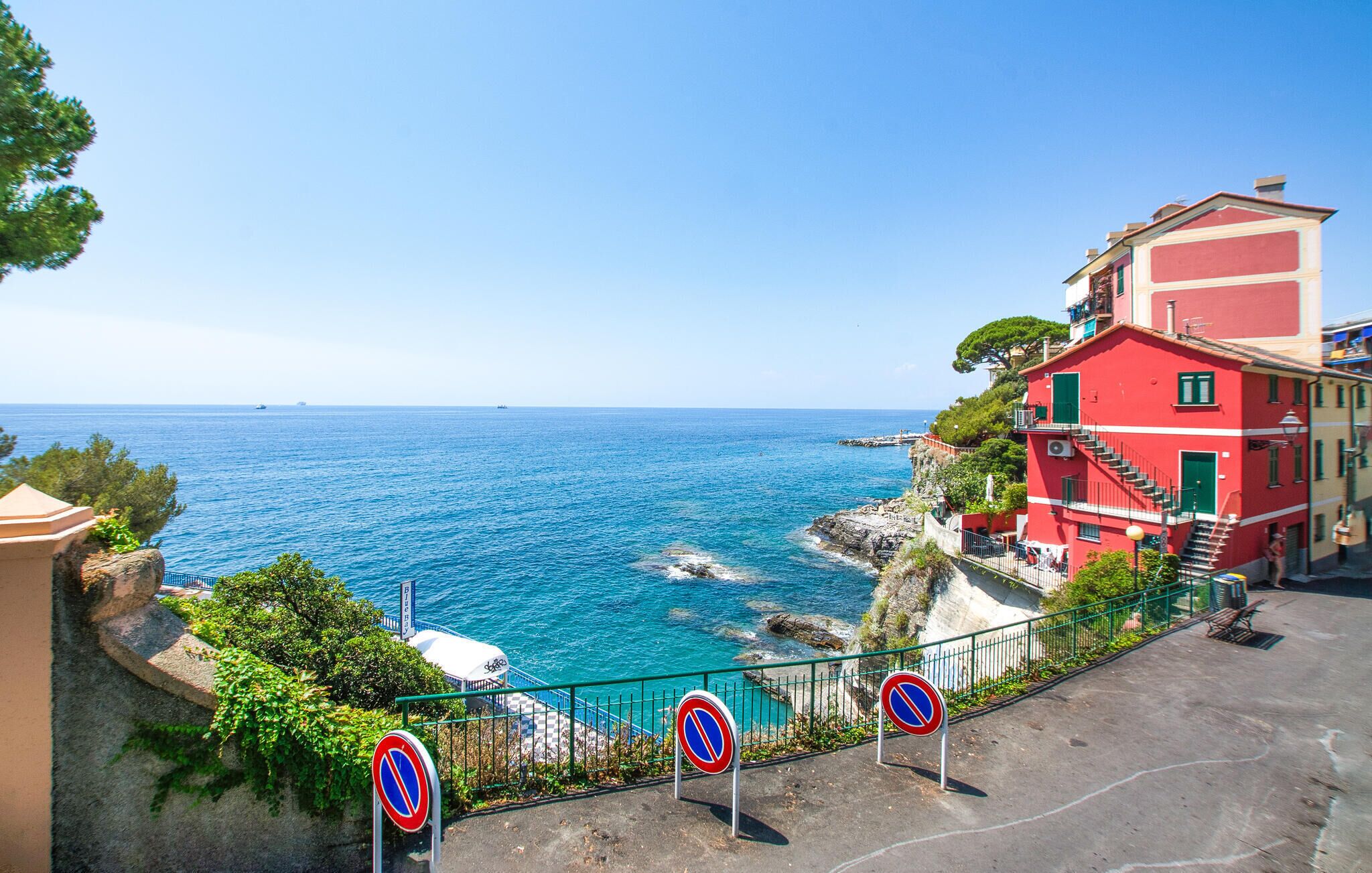 A coastal view with a red building, a clear blue sea, and a no parking sign.