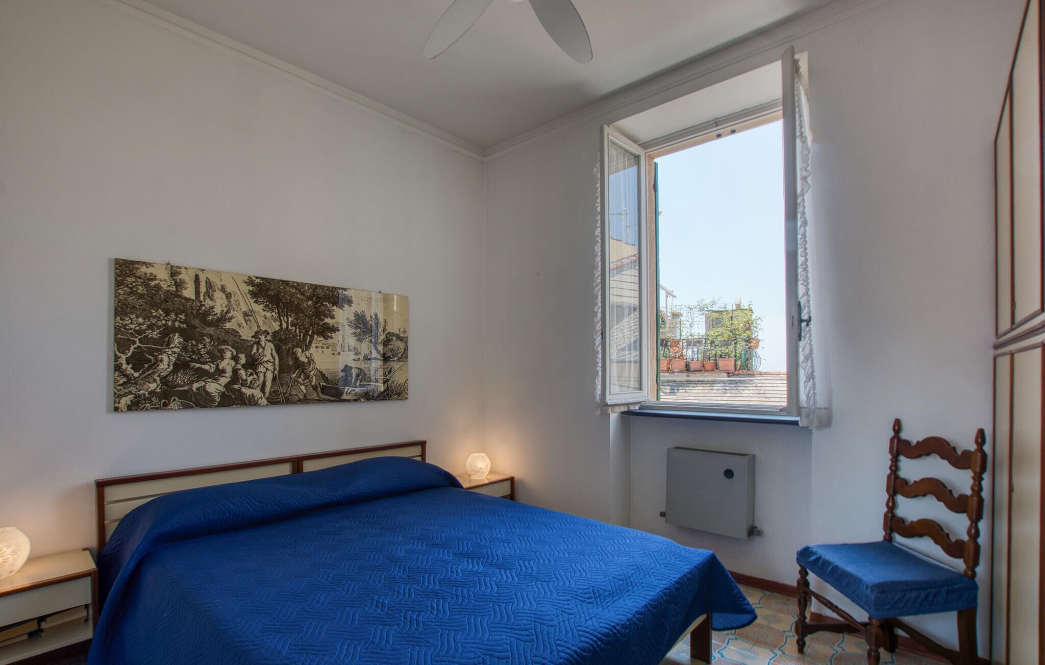 A bedroom with a bed, a nightstand, a chair, a window, and a radiator.