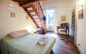 A bedroom with a wooden staircase, a bed with a green bedspread, a desk with a vintage radio, and a radiator.