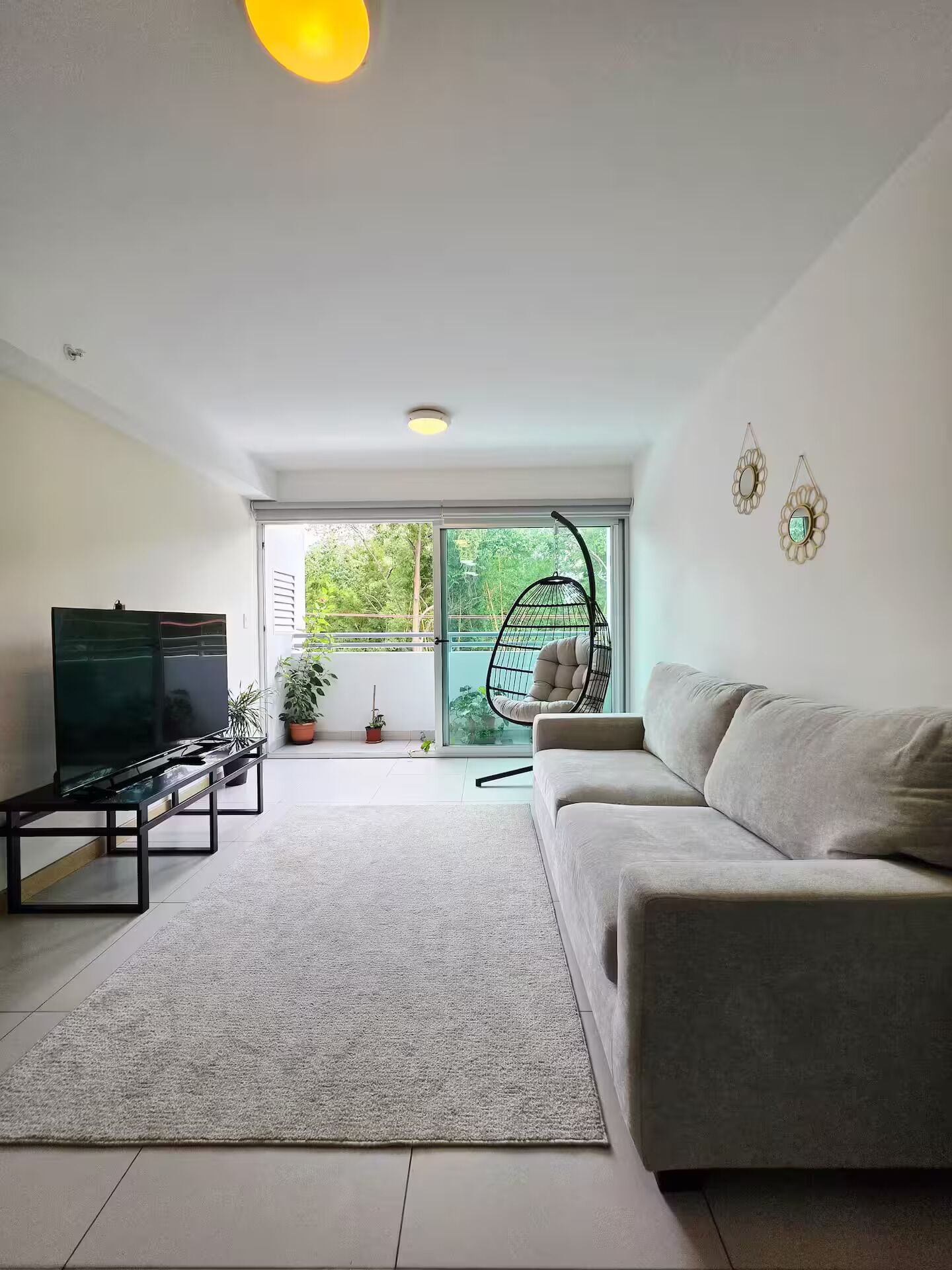 A modern living room with a sofa, a TV, a hanging chair, and a view of greenery outside.