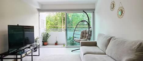 A modern living room with a sofa, a TV, a hanging chair, and a view of greenery outside.