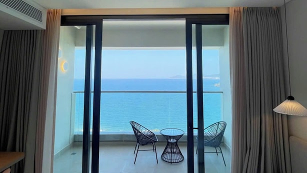 Une chambre d’hôtel avec un balcon, un lit, une table avec des chaises et une lampe.