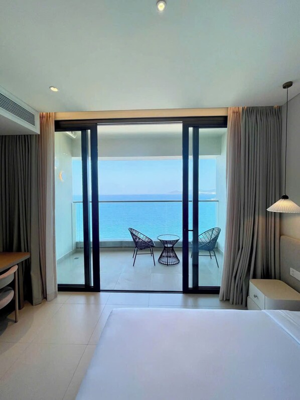 A hotel room with a balcony, a bed, a table with chairs, and curtains.