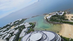 A coastal resort with a beach, a marina, and a modern hotel with a circular observation deck.