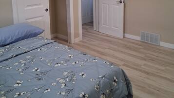 Un dormitorio con una cama, dos puertas, un perchero y una rejilla de ventilación.