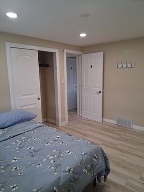 Un dormitorio con una cama, dos puertas, un perchero y una rejilla de ventilación.