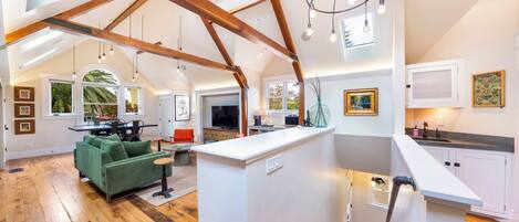 A spacious loft with high ceilings, exposed wooden beams, a central island, and a view of the outdoors.