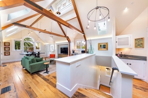 A spacious loft with high ceilings, exposed wooden beams, a central island, and a view of the outdoors.