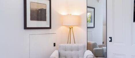 Une pièce comprenant un tableau encadré, un lampadaire, un miroir, une chaise et une petite commode en bois.