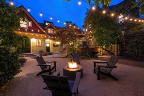 An outdoor seating area with a fire pit, surrounded by chairs and string lights.