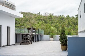 A rooftop terrace with a metal staircase, a potted plant, and a view of a forested hillside.
