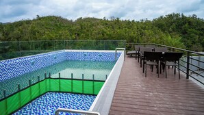 A swimming pool with a checkered tile pattern, surrounded by a wooden deck with chairs and a railing. - HORIZON MINH CHAU HOTEL (Van Don)