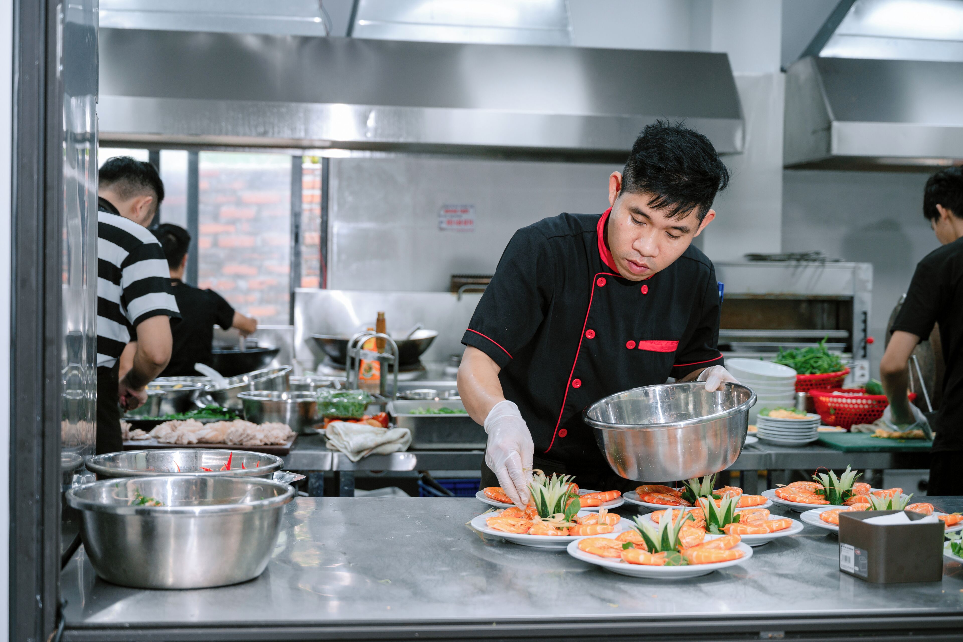Une cuisine équipée d’appareils électroménagers en acier inoxydable, et un chef qui prépare les plats.