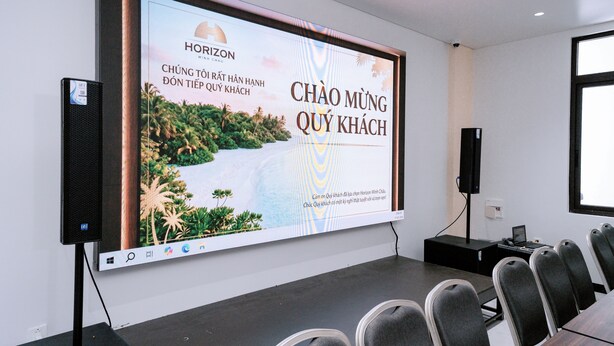 A conference room with a large screen displaying a presentation, a projector, a laptop, and rows of chairs. - HORIZON MINH CHAU HOTEL (Van Don)