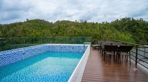 A swimming pool with a tiled edge, surrounded by a wooden deck and outdoor furniture.