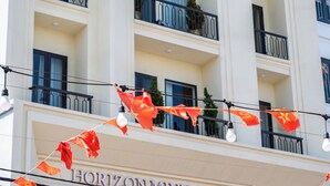 A hotel with multiple balconies, a sign reading 'HORIZON MINI CHAUMET,' and red flags hanging from the exterior. - HORIZON MINH CHAU HOTEL (Van Don)