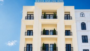 A multi-story hotel with a prominent entrance, balconies with railings, and a clear sky. - HORIZON MINH CHAU HOTEL (Van Don)
