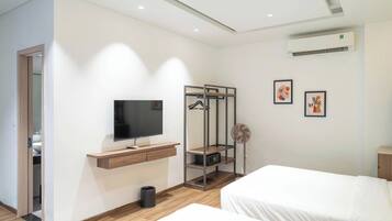 A hotel room with a flat-screen TV, a wooden desk, a hanging coat rack, a small fan, and two beds.